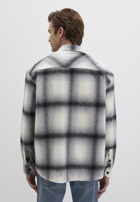Black and white plaid flannel shirt with long sleeves, buttoned cuffs, and a relaxed fit, showing a check pattern across the fabric.