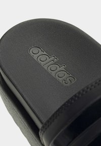 Sorte slidsandaler med tekstureret syntetisk overdel, der har et præg af 'adidas' logo. Blødt materiale og rund form, velegnet til afslappet brug.