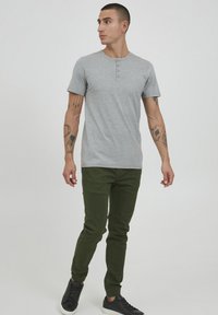 Gray short-sleeve henley shirt with a round collar and three buttons, paired with dark green tapered joggers and black sneakers.
