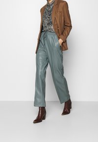 Blazer a cuadros marrón, blusa negra y blanca con volantes, pantalones de cuero en azul claro, y botas marrones de tacón con punta.