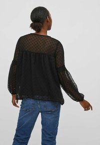 Černá průsvitná halenka s puntíkovaným vzorem, dlouhými nabíranými rukávy a nařasenými zády. Kombinováno s modrými džínami.