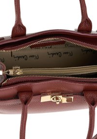 Bruine leren handtas met gouden draaiklemsluiting, twee handvatten en een beige stoffen interieur met een ritsvak en bedrukte voering.