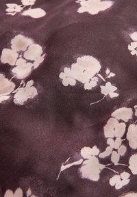 Un tessuto scuro presenta morbidi motivi floreali rosa di dimensioni variabili, mostrando una superficie liscia e uno sfondo a leggero gradiente.