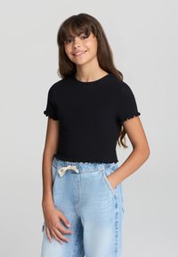 Czarny krótki T-shirt o żebrowanej fakturze i falbaniastych mankietach rękawów, w połączeniu z jasnoniebieskimi dżinsami z wysokim stanem z troczkiem.