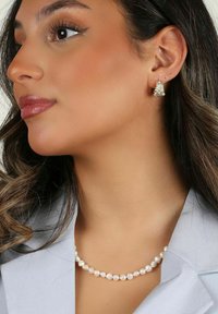 Elegant pärlarmband med pärlor, med en slät yta. Åtföljt av glittrande örhängen med floral design.