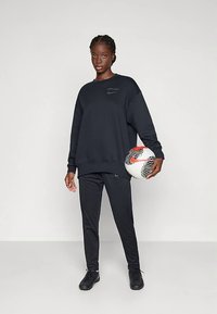 Fekete pamut pulóver környakú nyakkivágással, fekete sportnadrággal és fekete sportcipővel párosítva. Mintás focilabdát tart a kezében.