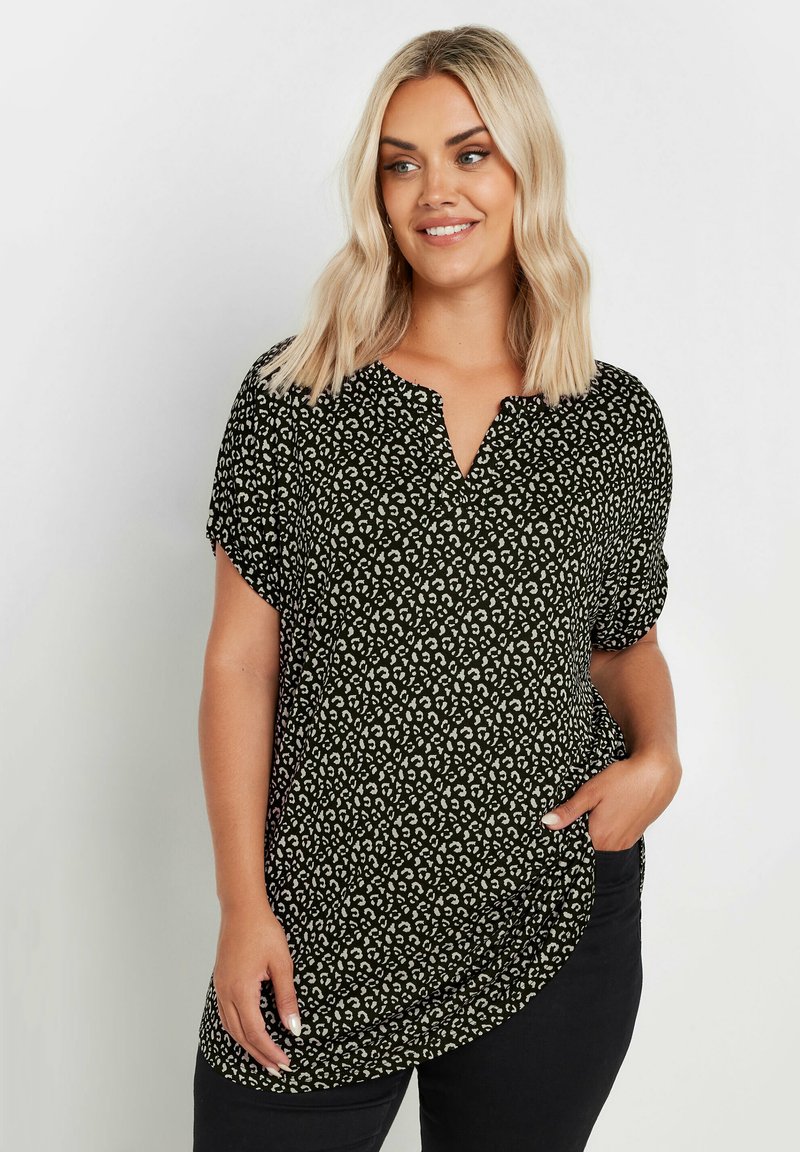 Musta ja vihreä kuviollinen blouse, jossa on lyhyet hihat, V-pääntie ja kaartuva helma, joka on valmistettu pehmeästä, textured-kankaasta.