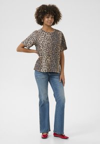 Leopard print short-sleeve top with a round neck, paired with light blue flared jeans and red flats. Smooth fabric texture, relaxed fit.