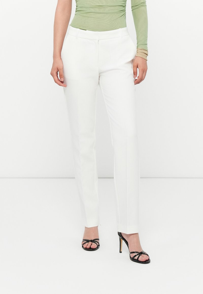 Witte tailor-made broek met een slim fit, gladde stof en strakke lijnen. Gecombineerd met zwarte hoge hakken en een lichtgroene top.