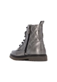 Botín de tobillo gris metálico con textura acolchada, cremallera lateral y cordones en el frente. Suela de goma resistente con acentos de marrón claro.