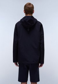 Marineblå hættejakke lavet af letvægtsstof, med en afslappet pasform, justerbar hætte og minimalistisk design. Bæres med matchende shorts.