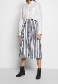 White long-sleeve shirt with two chest pockets paired with a black and white striped midi skirt featuring a button front and elastic waistband.