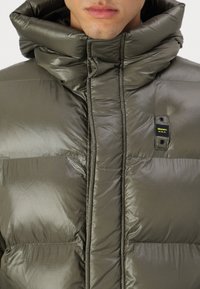 Puffer jacket in olive green, made from shiny, quilted material with a high collar and subtle horizontal stitching. Features logo tag.