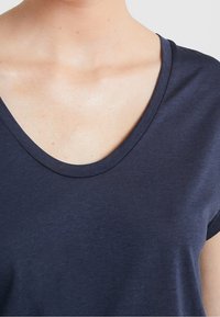 Námorně modré tričko s výstřihem do V vyrobené z měkké, lehké tkaniny s krátkými rukávy a hladkým povrchem, které se vyznačuje jednoduchým designem.