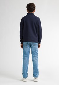 Polo a maniche lunghe blu navy, jeans azzurri e sneakers bianche con logo nero. Design semplice con colletto e vestibilità relax.