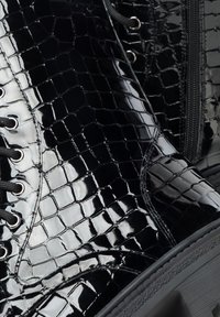 Lesklé černé kotníkové boty se vzorem krokodýlí kůže, s tkaničkami, kovovými průchodkami a viditelným bočním zipem na tlusté gumové podrážce.