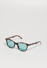 Occhiali da sole tartarugati con lenti azzurrate, forma quadrata e sottili aste nere con dettagli dorati e branding sulla tempia.