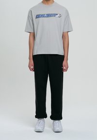 Szara koszulka z krótkim rękawem z niebieskim napisem "LOWLIGHTS" na klatce piersiowej. Połączona z czarnymi spodniami i białymi sneakersami. Prosty, luźny krój.