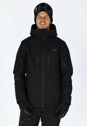 Schwarze wasserdichte Winterjacke mit Kapuze, ausgestattet mit Reißverschlusstaschen, elastischen Bündchen und einem schlanken Design. Handschuhe und Skibrille werden dazu getragen.