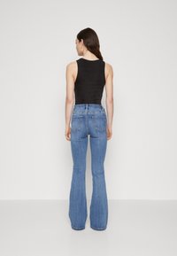Črn top brez rokavov v kombinaciji z modrimi širokimi jeans hlačami. Jeans hlače imajo zadnje žepe in visok pas. Gladek material s slabim raztegljivim učinkom.