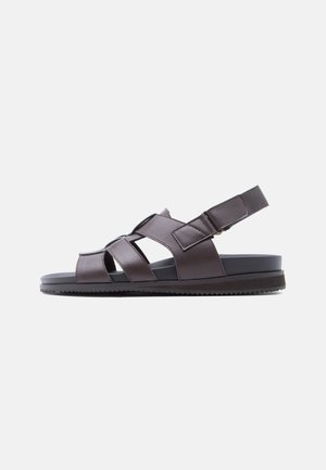 Sandalo da uomo in pelle marrone scuro con molteplici cinturini, cinturino regolabile alla caviglia e suola piatta nera, mostrato di profilo su sfondo bianco.