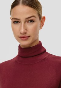 Burgunderfarbener Rollkragenpullover mit einer weichen, glatten Textur und einer körperbetonten Passform. Mit einem gerippten Halsausschnitt und einer schlichten Silhouette.