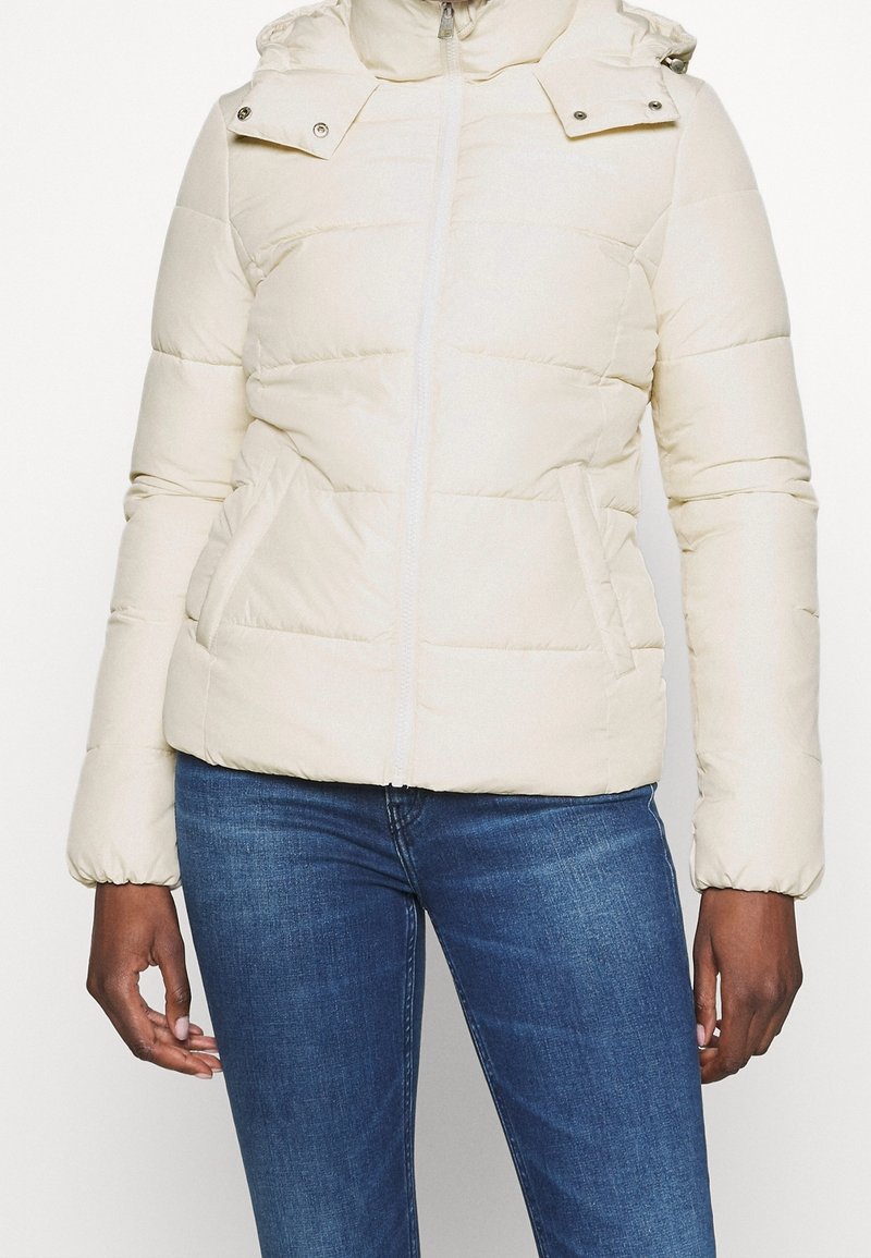 Giacca puffer beige chiaro con chiusura a zip, cappuccio regolabile e polsini elasticizzati. Presenta una trapuntatura orizzontale e tasche laterali.