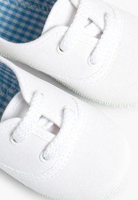 Scarpe da ginnastica bianche con superficie testurizzata, lacci bianchi e fodera interna a quadretti blu chiaro. Suola in gomma con leggero texture antiscivolo.
