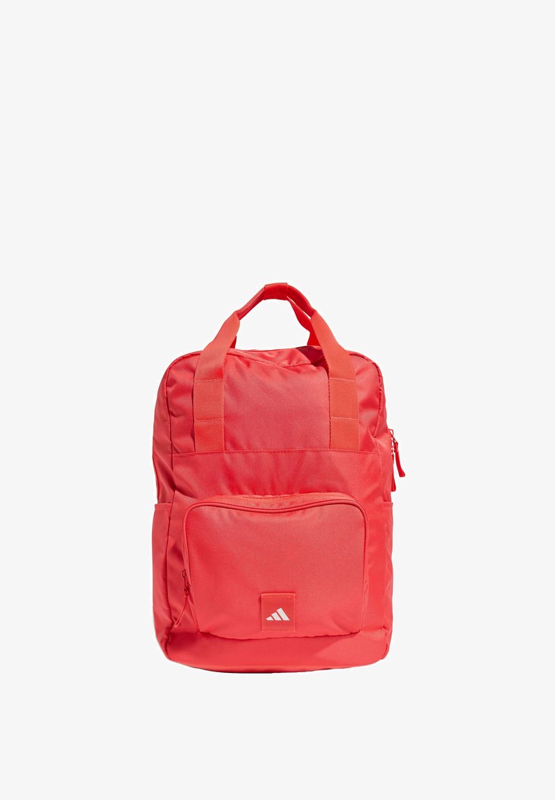 Zaino in tessuto rosso con due manici superiori, una tasca con zip frontale e dettaglio del logo. Presenta una trama liscia e una forma rettangolare.