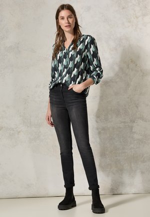 Blusa a maniche lunghe con una fantasia in nero, verde e bianco; abbinata a jeans neri aderenti e stivaletti neri alla caviglia. Design minimalista e tessuto leggero.