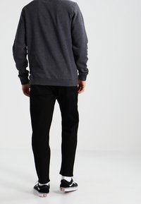 Harmaa collegepaita pyöreällä pääntiellä, mustat housut ja mustat tennarit valkoisilla yksityiskohdilla. Yksinkertainen malli, keskipainoinen kangas, rento istuvuus.