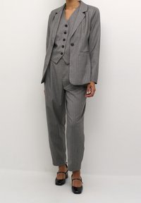 Grau gestreifter Anzug mit einem einreihigen Blazer, passender Weste mit fünf Knöpfen und tapered Hosen mit glatter Textur, kombiniert mit schwarzen Schuhen.