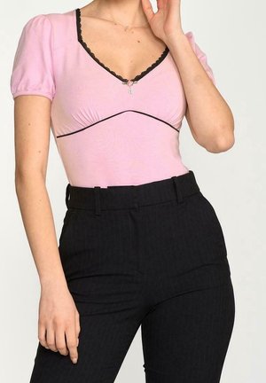 Vaaleanpunainen vartaloa myötäilevä paita liehukehihoilla ja mustalla pitsisomisteella, yhdistetty korkeavyötäröisiin mustiin pinstripe-housuihin. Mukana hienovarainen koristelu.