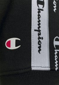 Tissu noir avec écusson du logo Champion en blanc et rouge, à côté de rayures verticales blanches et noires avec le texte répété "Champion" en noir et blanc.
