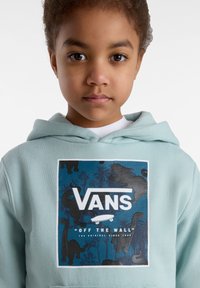 Ljusblå hoodie med ett grafiskt tryck av dinosaurier och palmträd. Framläggande logotext i vitt, med en stor svart kant som omger designen.