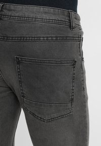Jeans de color gris oscuro con un bolsillo trasero estándar, un acabado texturizado sutil y costuras reforzadas a lo largo de las costuras.