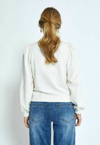 Pullover in crema chiaro con maniche a sbuffo, scollatura rotonda e orlo a coste, abbinato a jeans in denim blu a vita alta.