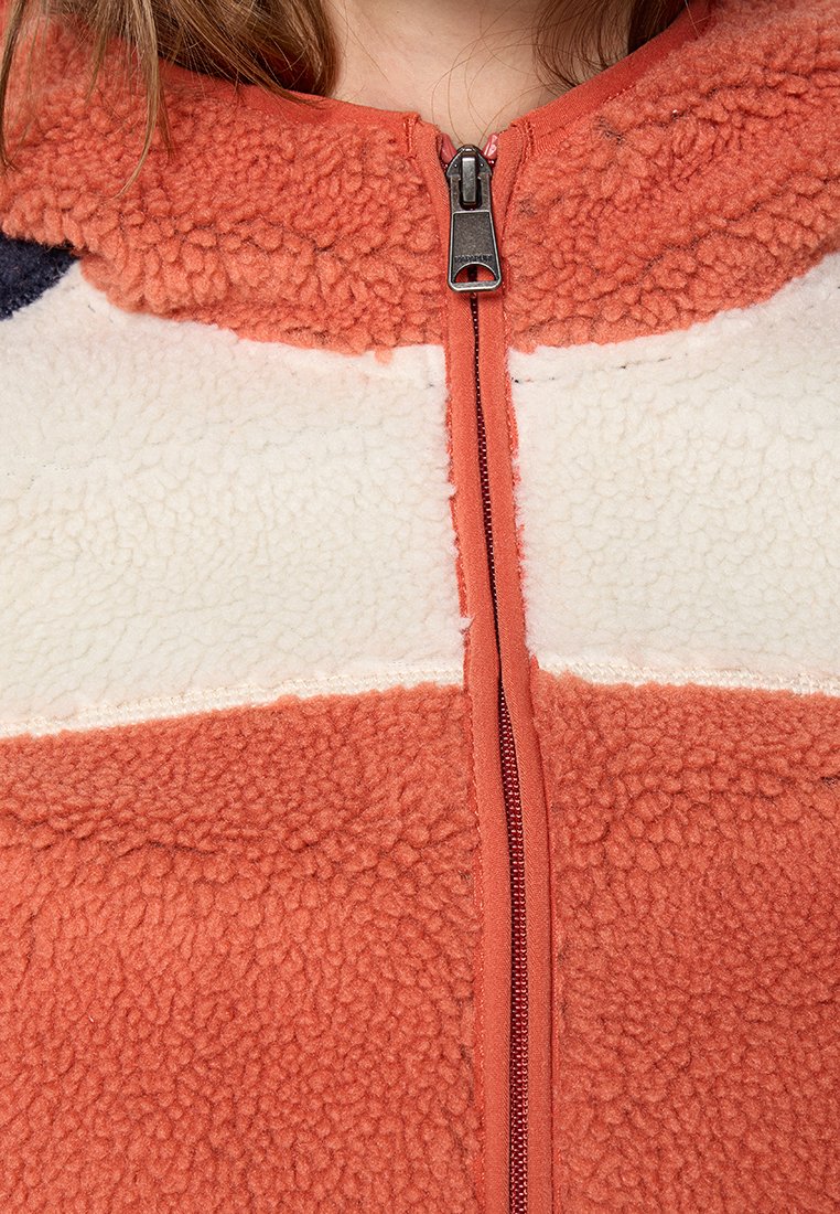 Chaqueta de forro polar en naranja y crema con una superficie texturizada, que presenta un cierre central y un diseño de cuello alto.