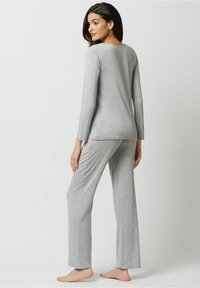 Pantaloni de pijama gri cu mânecă lungă, prezentând un top ajustat și pantaloni lejer în material moale și ușor. Design minimalist cu guler tip crew.