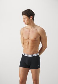 Bóxers negros de Nike con una cinturilla blanca de marca, confeccionados con un tejido suave, presentan un ajuste ceñido y una textura lisa, garantizando comodidad y soporte.