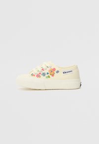 Gule kanvassneaker med hvit gummisåle, med fargerik blomsterbrodering på siden og metalløyer for snørebåndene.
