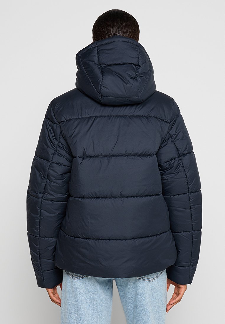 Marineblaue Steppjacke mit Kapuze, gestepptem Design und leicht oversized Passform. Sanfte Textur mit horizontalen Steppdetails.