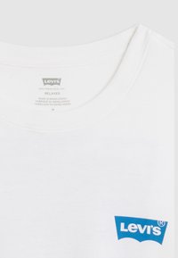 Baltas medvilninis marškinėlių su apvalia apykakle modelis su mėlynu Levi's logotipu kairėje krūtinės pusėje. Viduje esantis etiketas nurodo laisvą siluetą, dydį M, pagaminta Bangladeše.