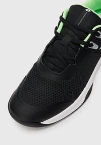 Schwarzer und grüner Sportschuh mit Mesh-Obermaterial, schwarzen Schnürsenkeln und weißer Sohle, aus einer oberen Vorderansicht gezeigt.