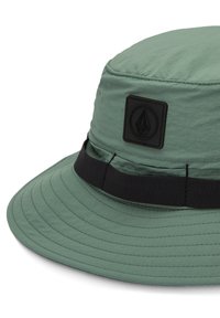 Chapeau seau vert en tissu léger, avec une bande noire et un patch logo texturé à l'avant. Large bord courbé.