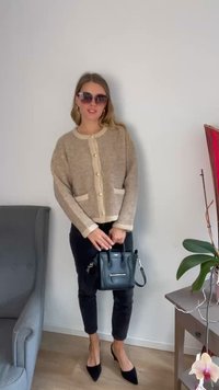 Beige strikkegenser med kremfargede detaljer og knapper, parret med svarte tettsittende bukser og spisse svarte hæler, som holder en liten svart veske.