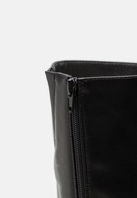 Fekete bőr bokacsizma sima textúrával és oldalsó cipzárral. A design ívelt nyílással és szilárd formával rendelkezik.