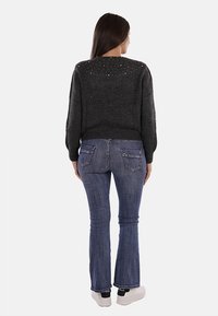 Maglione grigio scuro con sottili dettagli in strass sulla spalla, abbinato a jeans blu a zampa d'elefante e sneakers bianche.