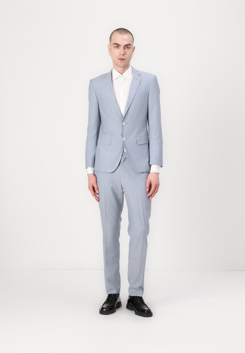 Traje azul claro hecho de una tela suave, con un diseño de un solo botón, solapas de muesca y zapatos negros. Ajuste limpio y entallado.