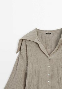 Lichtbruine linnen shirt met een textuur, gekreukeld ontwerp, brede kraag en vijf knopen sluiting. Heeft losse mouwen met zijslieten.